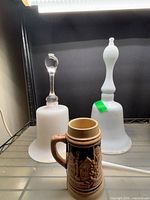 Two milk glass bells and ceramic stein on shelf