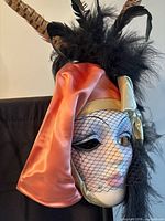 Front view of mask showing satin drape, veil and feather headdress