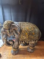 Left side view of ornate elephant statue showing gold saddle blanket and tassels