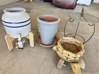 Group shot showing all four items: ceramic crock on stand, gray planter on saucer, wooden turtle planter, metal sundial on stand