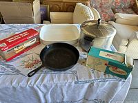 Group shot of all five items: boxed Hamilton Beach electric knife set, boxed food chopper, cast iron skillet, white ceramic baking dish, aluminum stock pot with lid