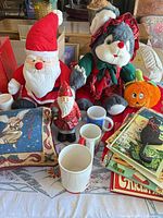 Overview showing plush Santa, plush cat, wooden Santa, mugs, pillow, books, pumpkin frame