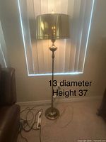 Full view of brass floor lamp beside chair, visible power strip, height and diameter text overlay