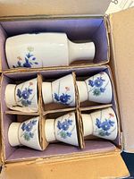 Open box showing carafe and six cups in cardboard dividers