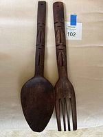 Front view of carved wooden spoon and fork showing tiki motif and overall wear
