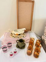 Overview of lot showing calendar frame, gravy boat on platter, creamer with saucer, striped glasses, amber leaf tumblers, and salt & pepper shakers
