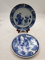 Two blue-and-white plates displayed together, Chinese dish on stand, souvenir plate flat