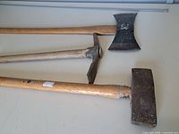 Top-down view of axe, pickaxe and sledge hammer showing full length and heads