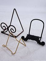 Three display stands: gold twisted wire, black ornate, brown triangular scroll