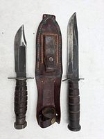Two combat knives and leather sheath laid out