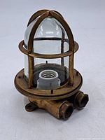 Angled view showing brass cage, glass globe, conduit ports, socket