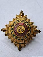 Front view of gold-tone starburst badge showing enamel details and central shields