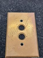 Front view of brass push-button switch plate showing holes and surface wear