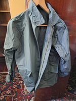 Front view of gray-green waterproof jacket on hanger showing zipper, pockets, collar