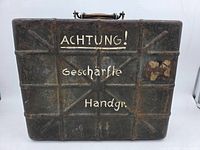 Front of metal crate showing "ACHTUNG! Geschärfte Handgr." text and ribbed structure