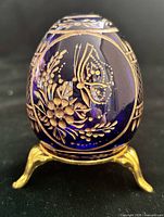 Front view of cobalt blue glass egg on gold-tone stand showing butterfly and floral gilt design
