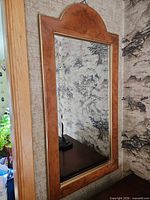Full view of mirror on wall showing rectangular shape with arched top and wood veneer frame