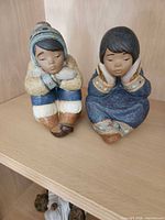 Front view of both Lladró Inuit child figurines seated on shelf