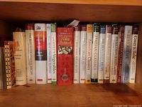 Row of white-spined America’s Test Kitchen / Cook’s Illustrated hardcovers with red and green titles, plus Joy of Cooking and Cover & Bake