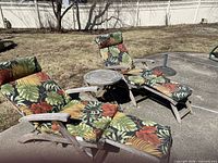 Two teak chaise lounges with tropical cushions and small round teak side table as seen outdoors