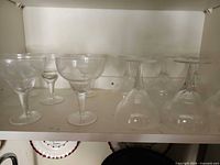 Six clear glass coupes on cabinet shelf, mix of upright and inverted