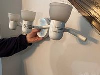 Front view of 3-light vanity fixture held against wall, showing white finish and frosted glass shades