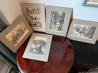 Five matted black-and-white engravings displayed on tabletop