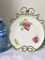 Front view of Belfor Grapes porcelain plate beside water bottle for scale