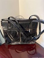 Front view of black leather BACI tote with double handles and exterior zip pocket
