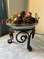 Angled view of glass bowl on black metal scroll stand filled with autumn botanicals