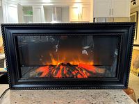 Front view with flame effect active, showing decorative framed glass and faux logs