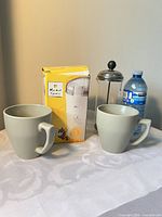 Front view showing two gray mugs, Market Square grinder box, French press and water bottle for scale