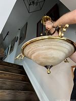 Hand holding large brass-tone chandelier showing overall size and dome