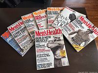 All eight Men’s Health magazines laid out on table showing covers