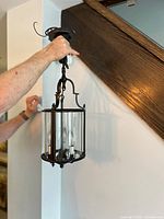 Full view of fixture held against wall showing overall form, chain, canopy, cylindrical glass body and metal frame