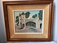 Framed painting depicting stone gatehouse and arched bridge, wood frame with linen matting