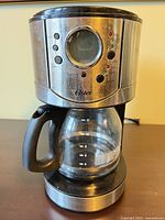 Full view of Oster coffee maker showing stainless steel body, controls, and glass carafe