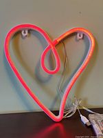 Front view of illuminated heart sign showing shape, color, frame, keyhole hangers and cables