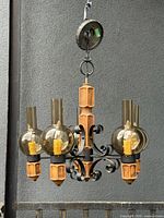 Full view of chandelier hanging, showing iron scrolls, wood elements, five smoked glass globes and canopy