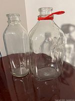 Front view showing both glass bottles—rectangular embossed eagle bottle with red spout and cylindrical plain bottle