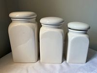 Front view of three white ceramic canisters in graduated sizes