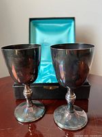 Two silver-plated goblets standing in front of presentation box