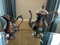 Front view of teapot and creamer showing ornate handles, spouts, lid, bases