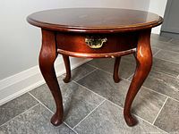 Full view of round side table with cabriole legs and drawer