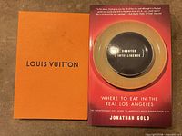 Front view of book next to Louis Vuitton envelope/box