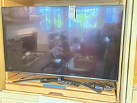 Front view of LG 49" TV on stand with remotes and Roku visible