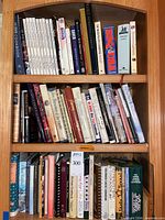 Two shelves filled with assorted cookbooks showing variety of bindings and subjects