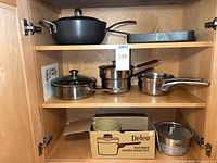 Cabinet shelf with black sauté pan, square grill pan, stainless saucepans, Deleo box