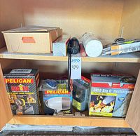 Cabinet shelf with boxed Pelican Big Ed, Pelican Professional angle light, Pelican 3850 Big D kit, cardboard box of hitch, additional packaged flashlight visible