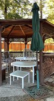 Full view of patio furniture under gazebo including round tables, square table, chairs, umbrella